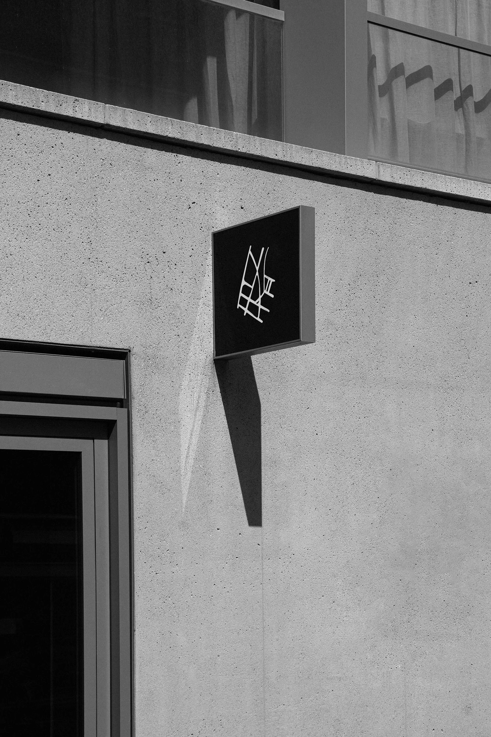 Black and white architectural shot featuring a building exterior with a geometric sign and a window, creating a minimalist urban scene.