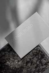 Embossed business card resting on a dark textured stone against a neutral paper backdrop with soft shadows
