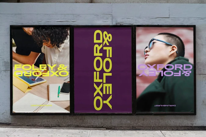 Outdoor billboard display featuring two people working on an iPad and a stylish person wearing glasses in an advertisement for Oxford & Foley.