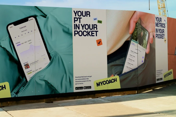 Phone displays MyCoach app in jacket pocket on advertisement for fitness program; health, workout, and food tracking.