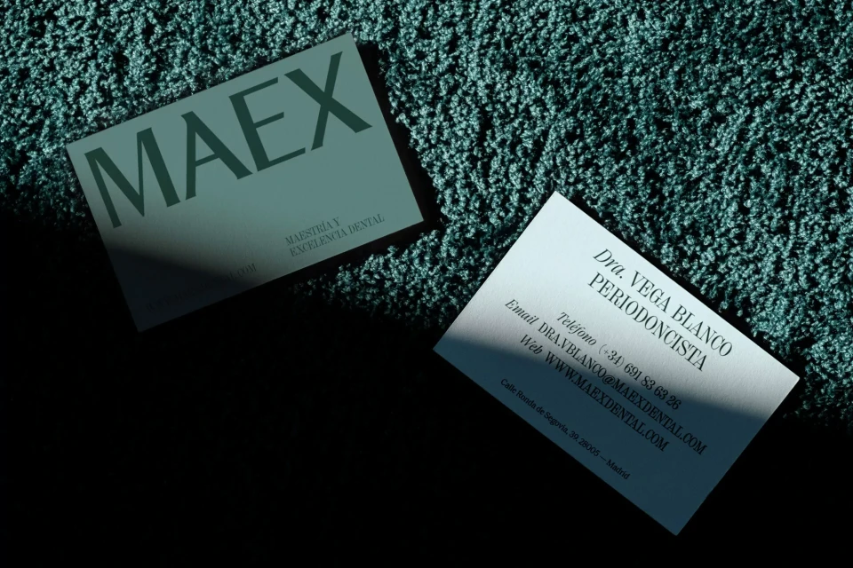 Two business cards on a teal, textured surface, one with the company name MAEX, highlighting dental excellence.