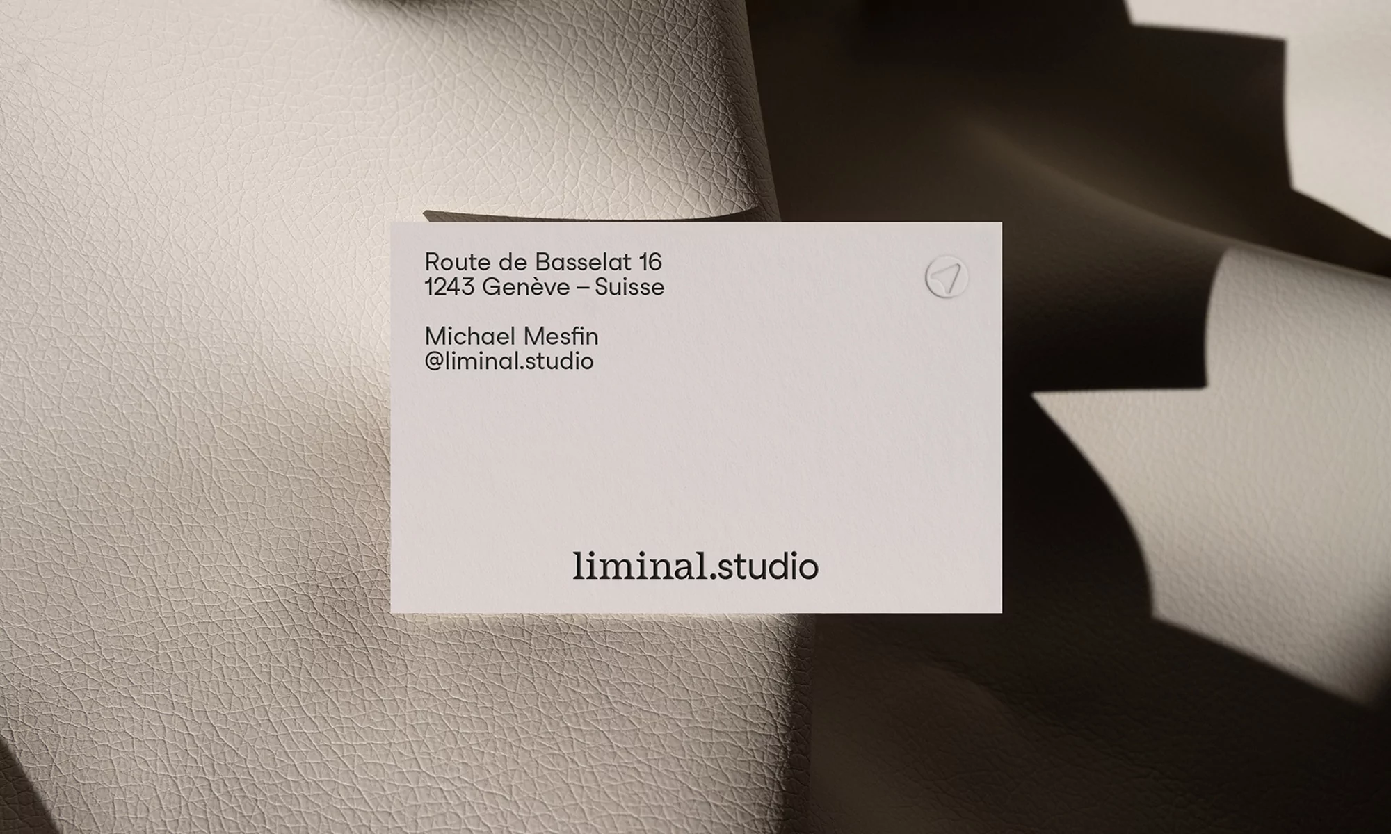 Close-up of a white business card on a textured leather surface, featuring the logo and contact information for liminal.studio.