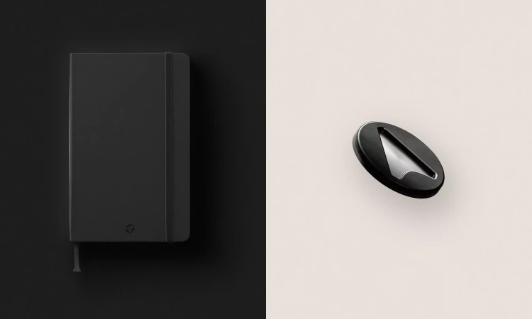 Monochrome flat lay of a closed black notebook with elastic closure beside a black and silver metal object on a split background.