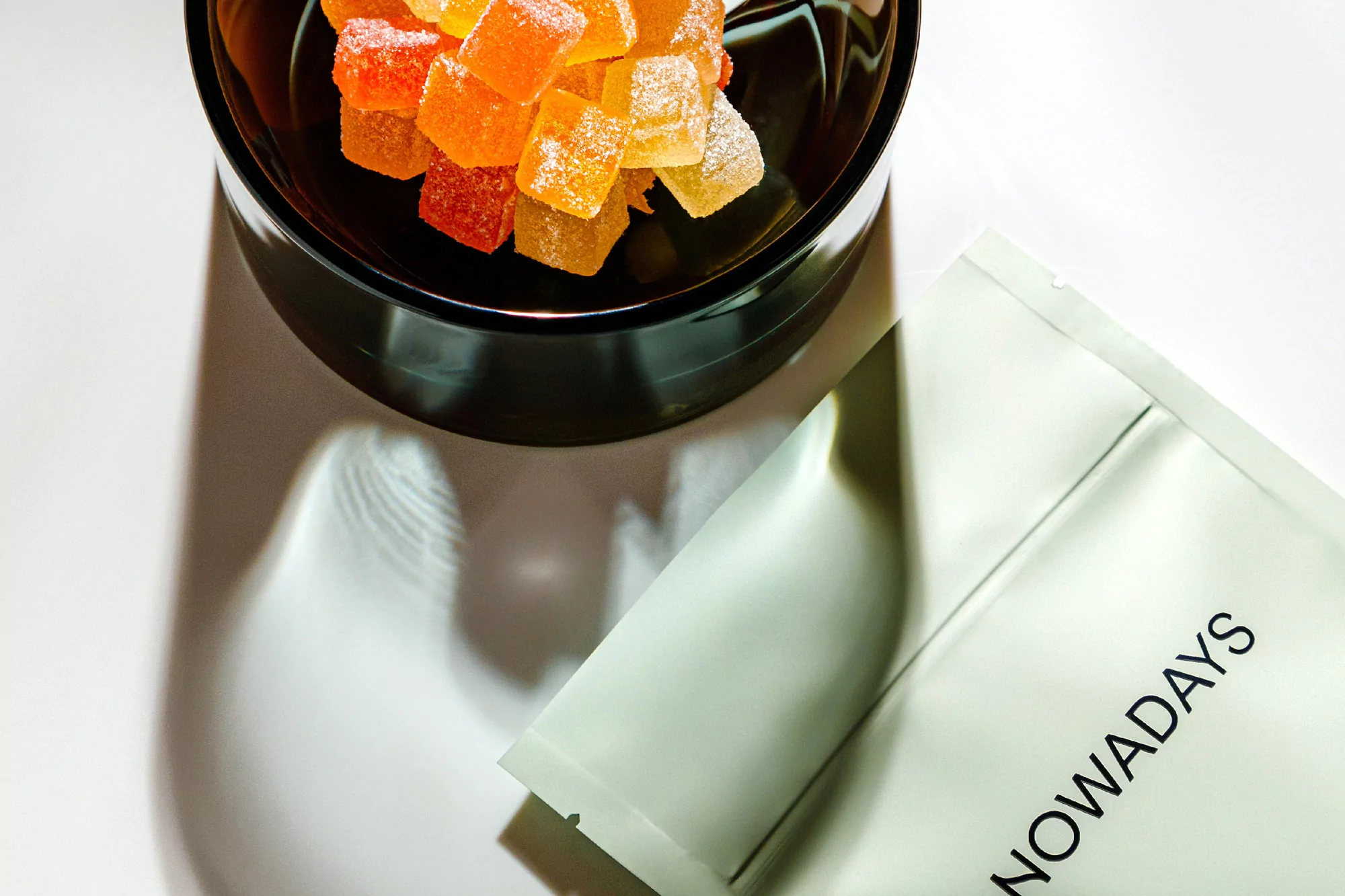 Close-up of gummy candies in a black bowl next to a product package, showcasing a minimalist food presentation on a white background.