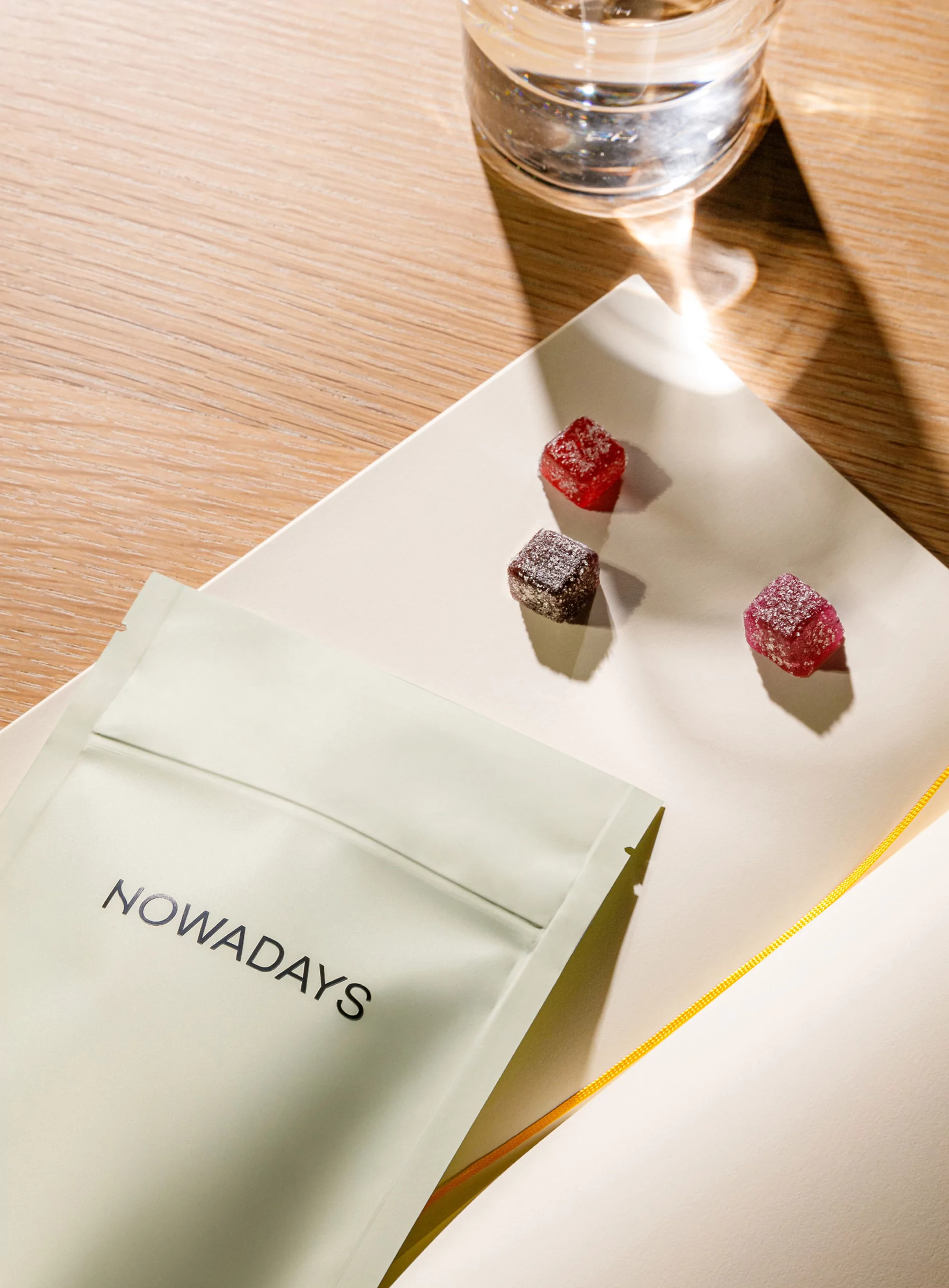 Gourmet edibles presented on a white plate next to a glass of water and a branded package on a wood surface in soft lighting.