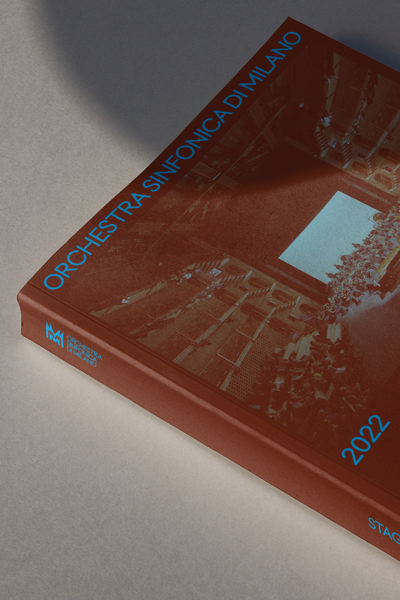 Red hardcover book titled 'Orchestra Sinfonica di Milano 2022' on a white surface with a shadow; the cover features a concert hall.