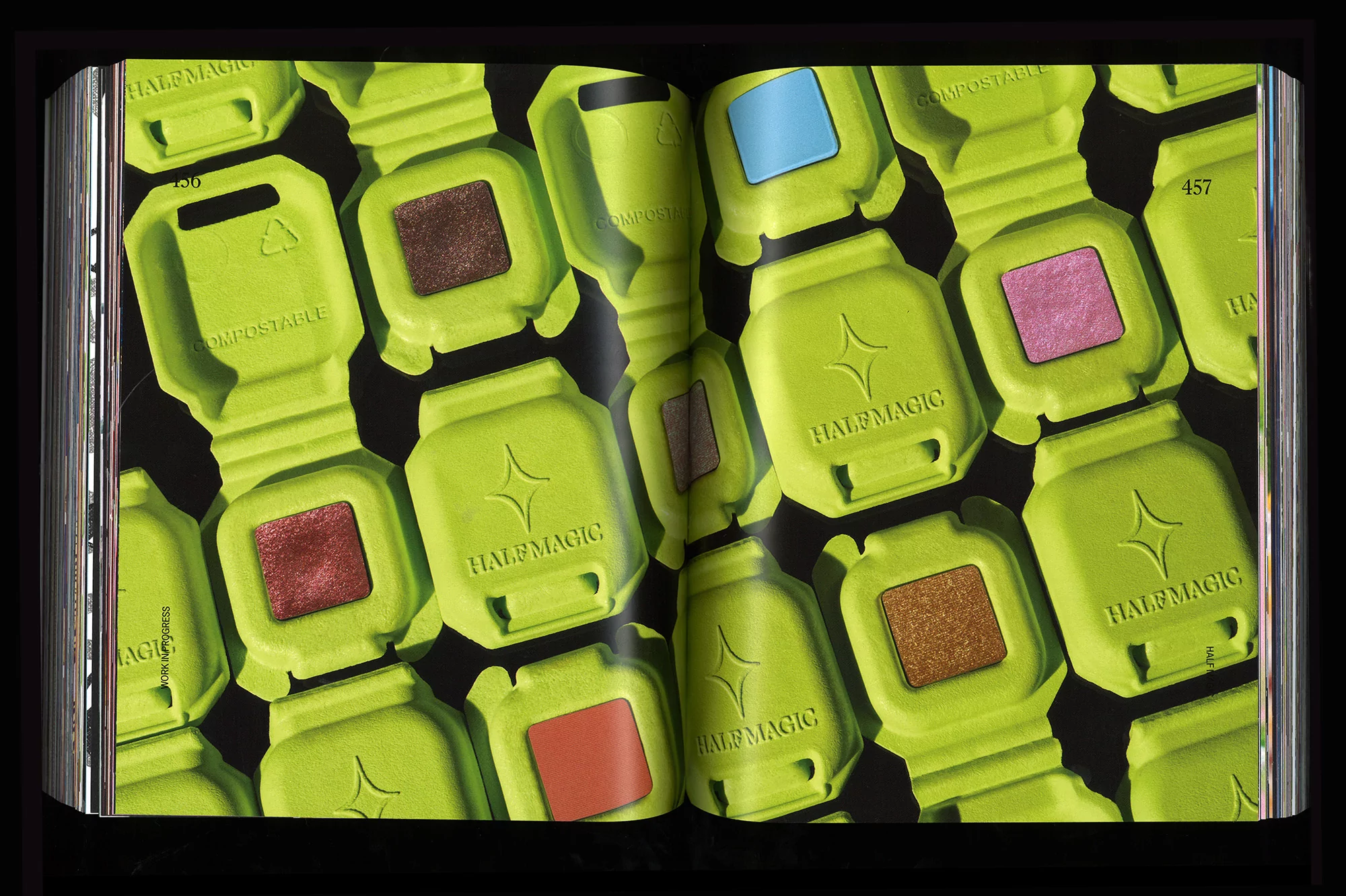 Open book spread featuring colorful cosmetic compacts with 'HALF MAGIC' branding, arranged on a black background for beauty product promotion.