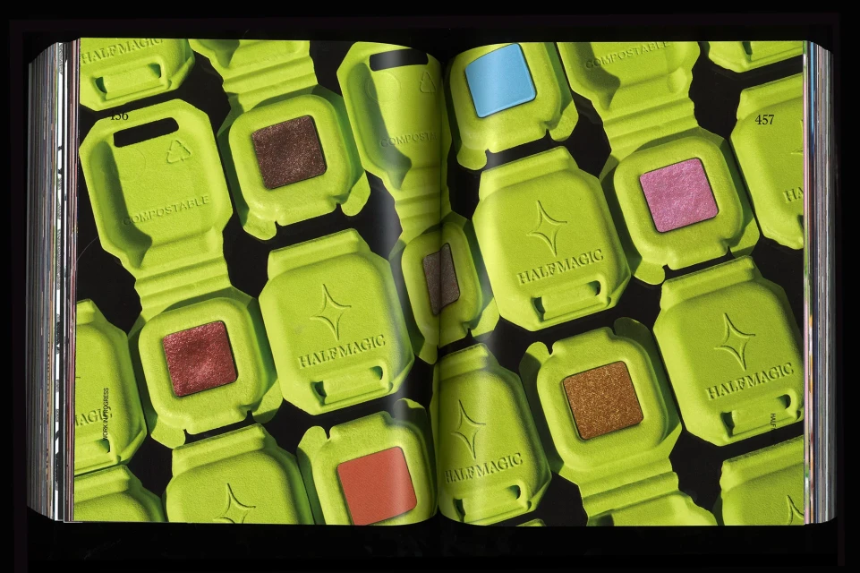 Open book spread featuring colorful cosmetic compacts with 'HALF MAGIC' branding, arranged on a black background for beauty product promotion.