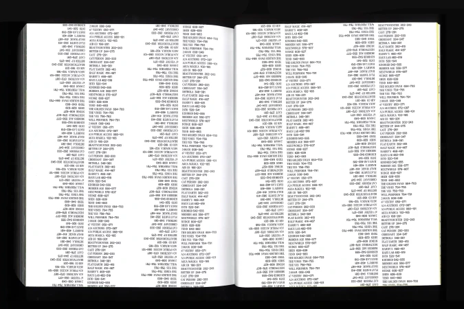 Open book shows densely-packed pages filled with black text arranged in columns, set against a black background. Focus is on readability.