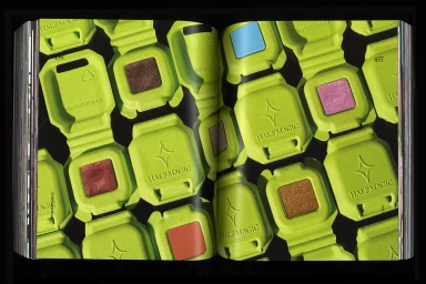 Open book pages featuring a repeating pattern of lime green compostable makeup packaging cases against a black background.