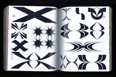 Open book page displaying a collection of dark geometric graphic design symbols and abstract shapes on white paper.