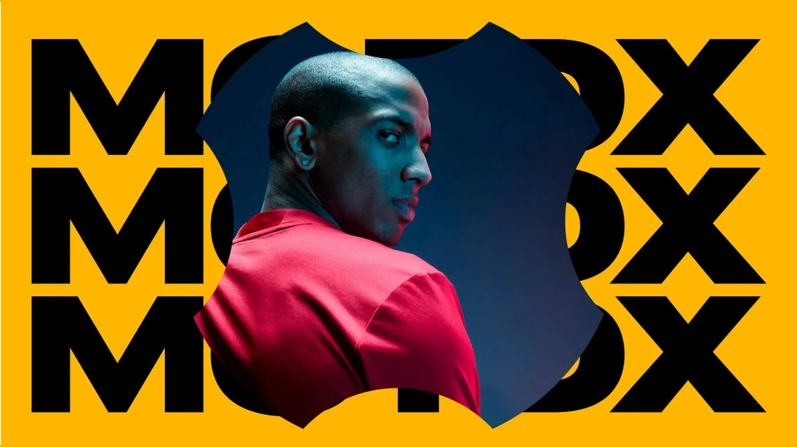 Close-up portrait of a bald adult male in a red shirt, looking over his shoulder, against a yellow and dark blue patterned background.