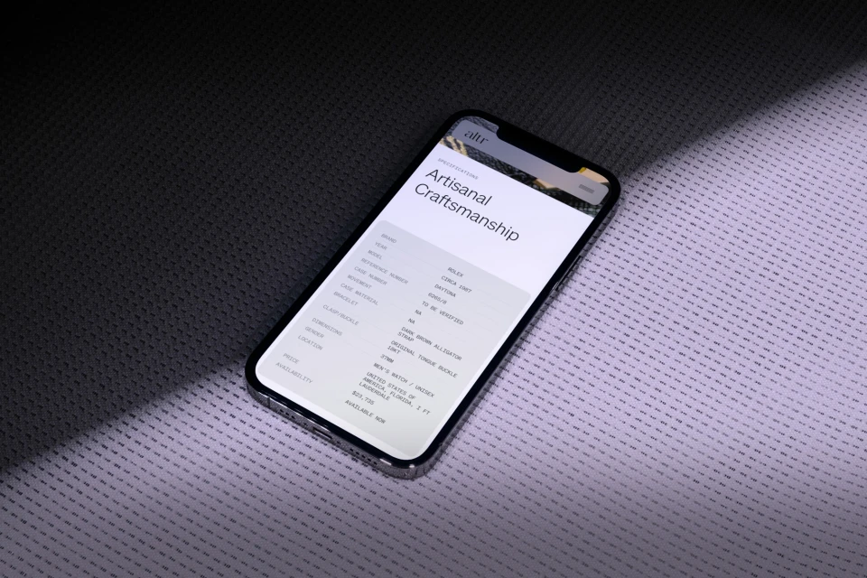 An iPhone displays an article about artisanal craftsmanship on a textured gray surface in studio lighting, creating a high-tech, sleek composition.