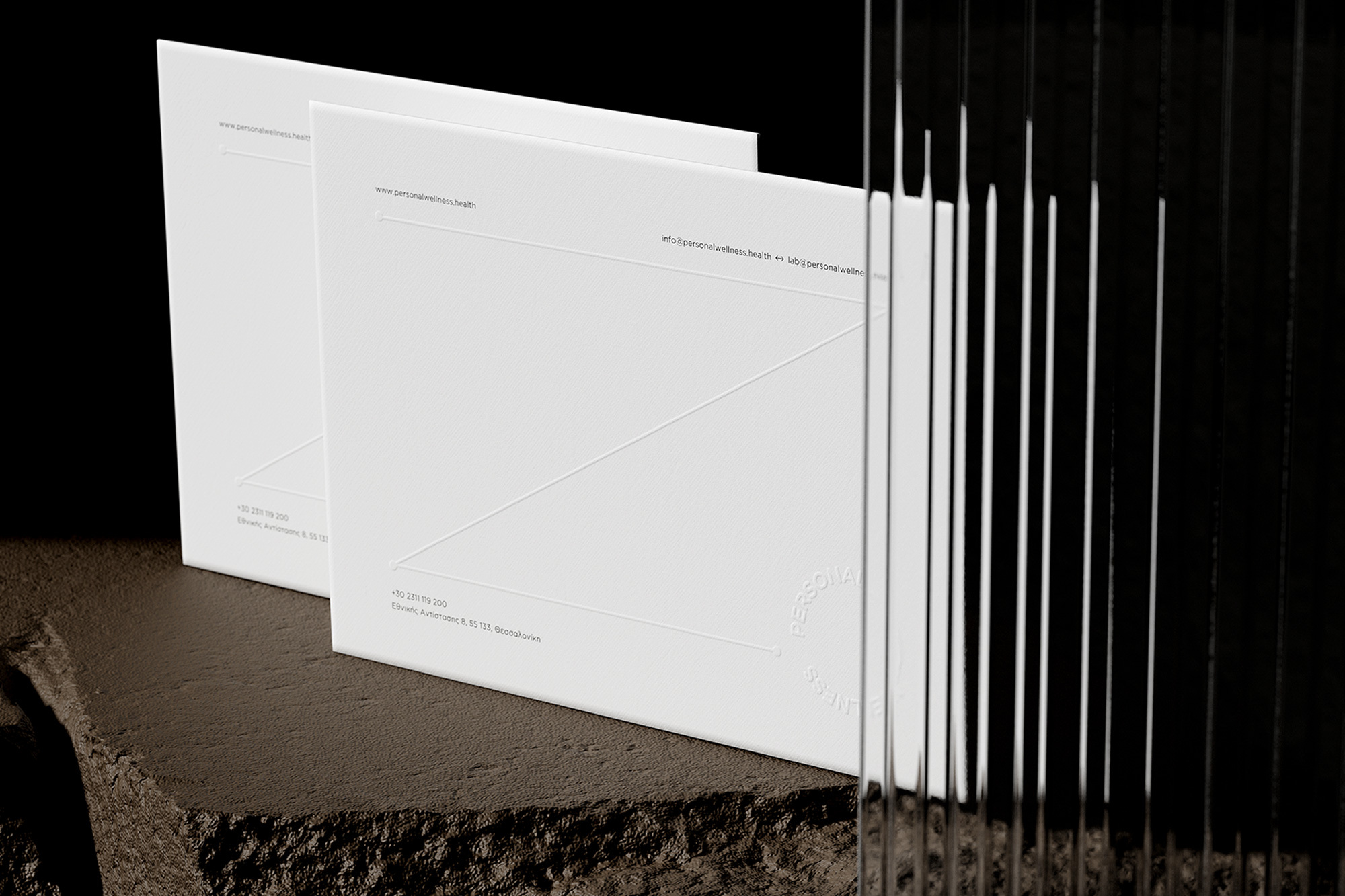 Two white cards stand on a rough stone surface, with a linear glass structure casting shadows, creating an abstract and minimalist composition.