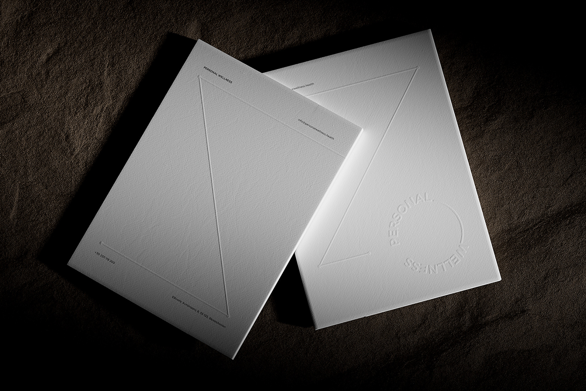 Two white personal wellness brochures featuring minimalist triangle and circle designs, displayed on a textured grey background.