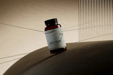 Amber glass supplement bottle with a white label reading SPECTRUM, tied with fine string across a neutral textured background