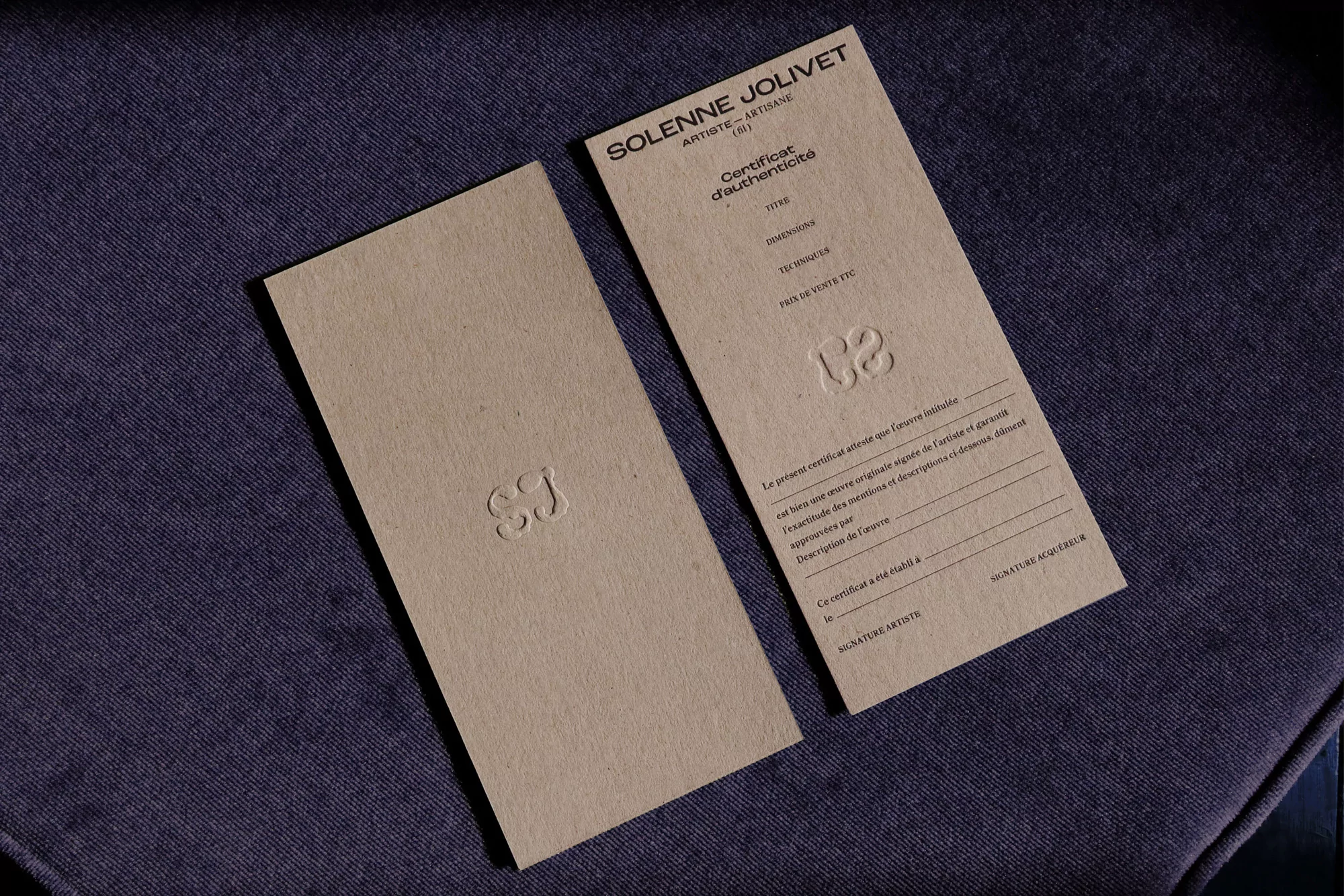 Two light brown, rectangular certificates with embossed text and logos lay diagonally on a textured blue surface under studio lighting.