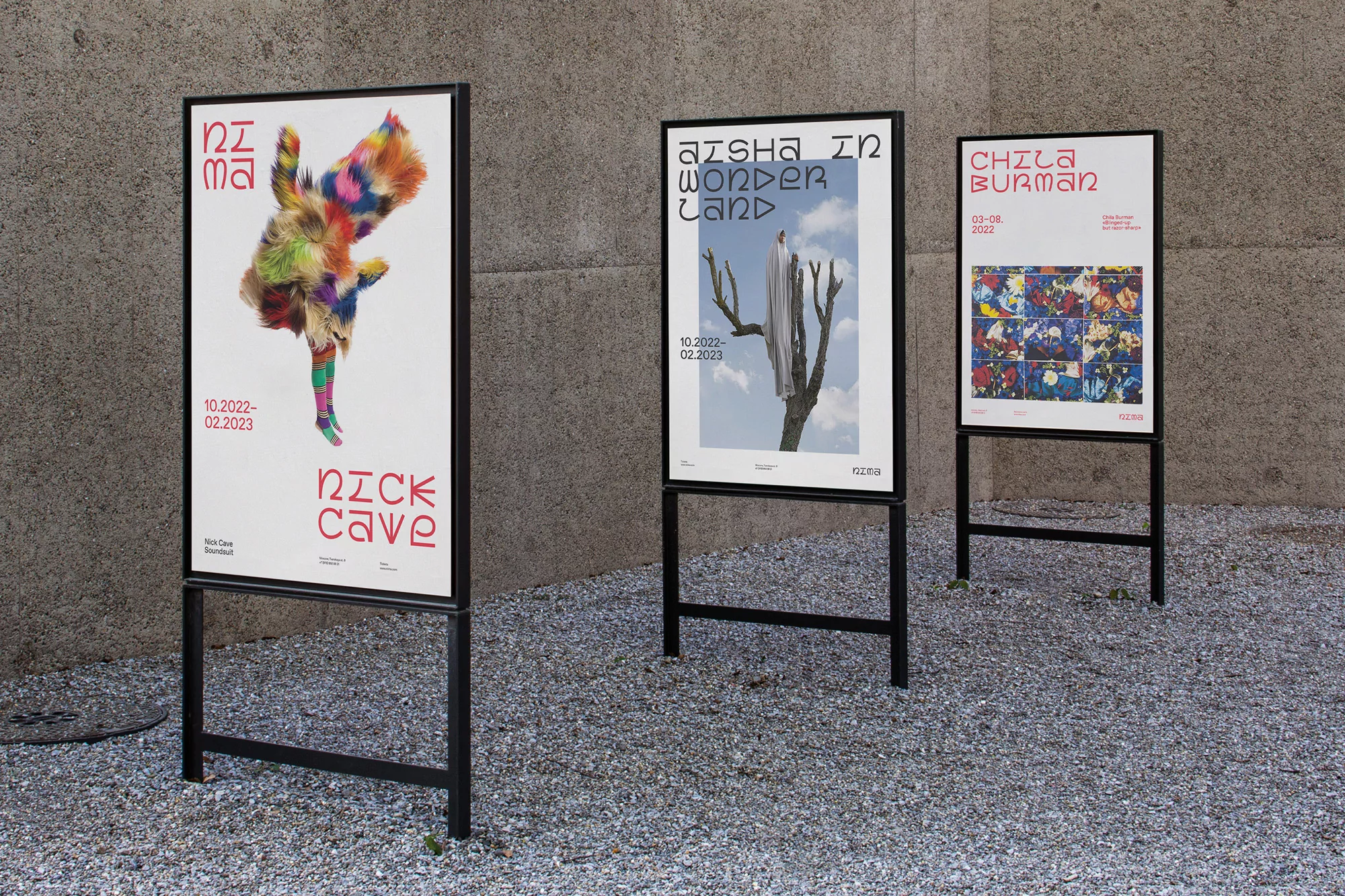 Outdoor view of three art exhibition posters in black frames featuring colorful graphic designs and clear typography on white backgrounds.
