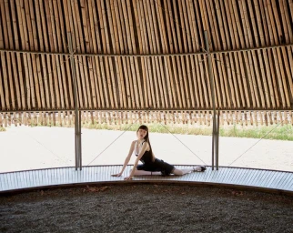 Model seated on a curved wooden platform under a bamboo dome structure for Noblesse Korea photographed by Xiuyu Chang.