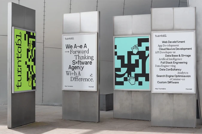Outdoor view of Turntabl brand advertisements on display stands, featuring text-based graphics and branding in a city setting.