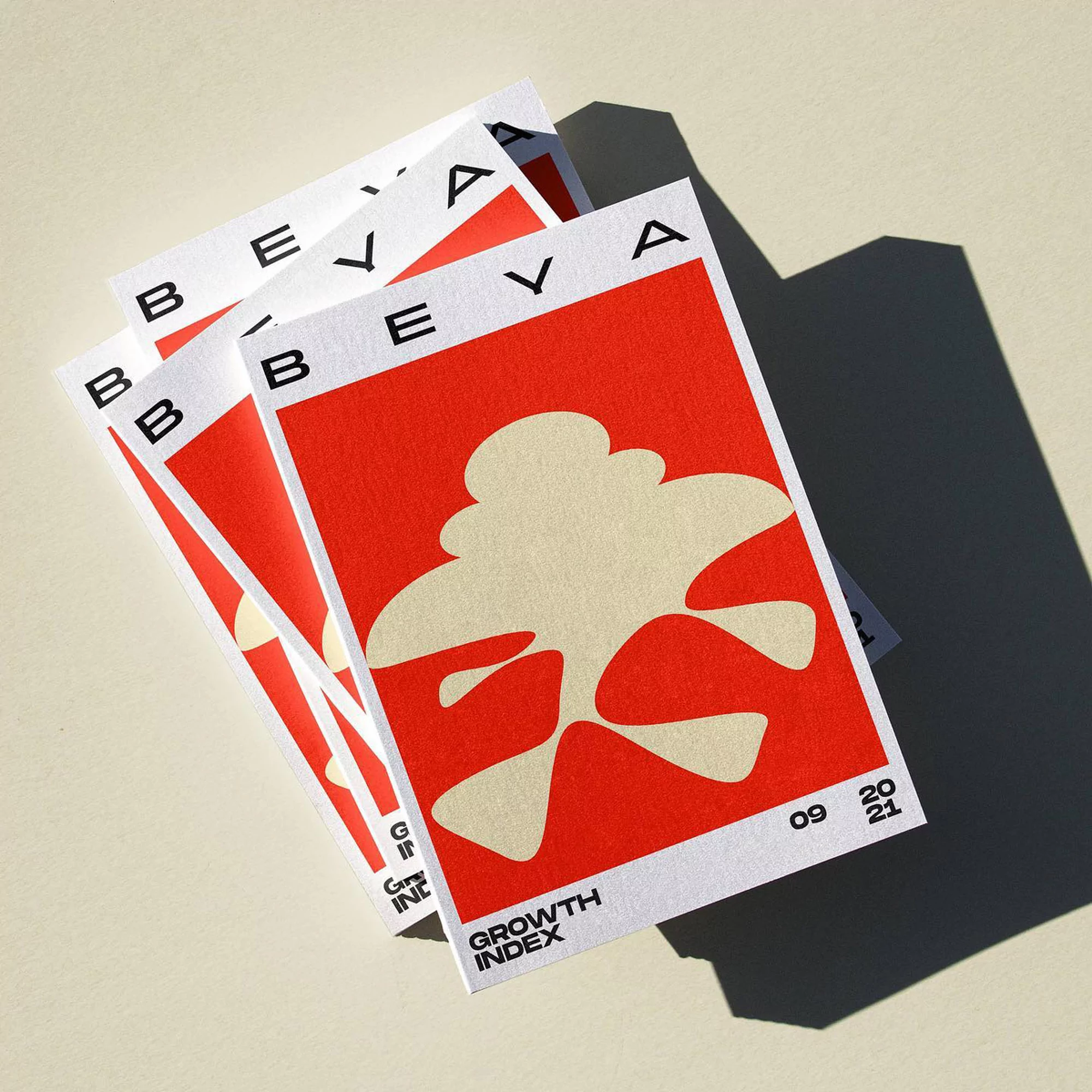 Abstract posters with 'BEVA' text, red and beige color scheme, geometric design, stacked composition with drop shadow on a light surface.