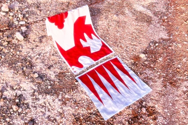 Red and white patterned textile pieces resting on a rough gravel and stone ground next to a metal chain.