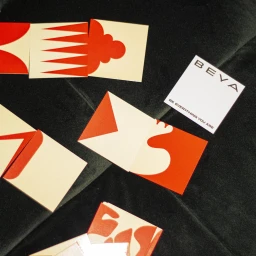 BEYA brand identity graphic design collateral with red and cream cards on dark velvet fabric.