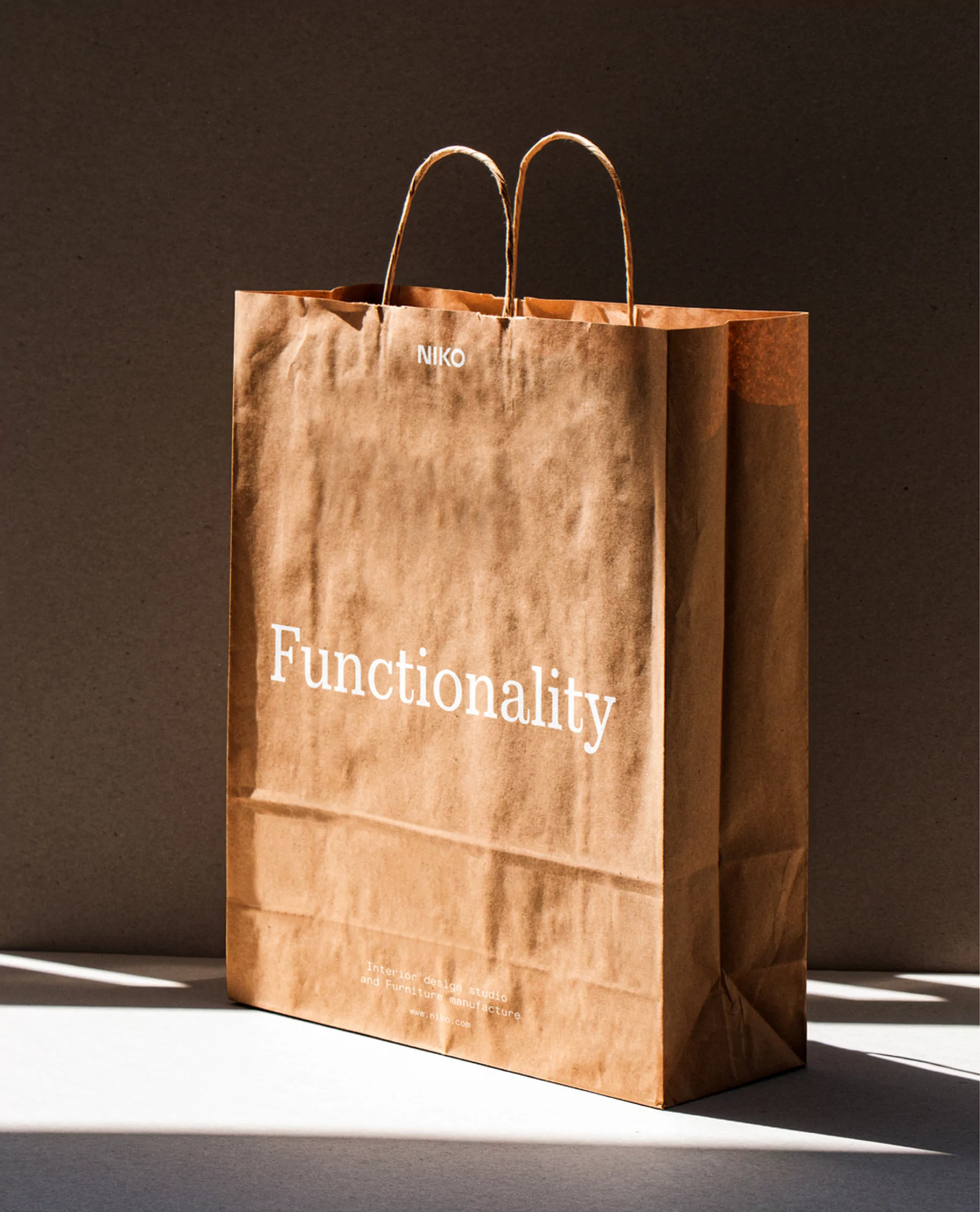Studio shot of a brown paper shopping bag with handles against a neutral background. The word 'Functionality' is printed on it.