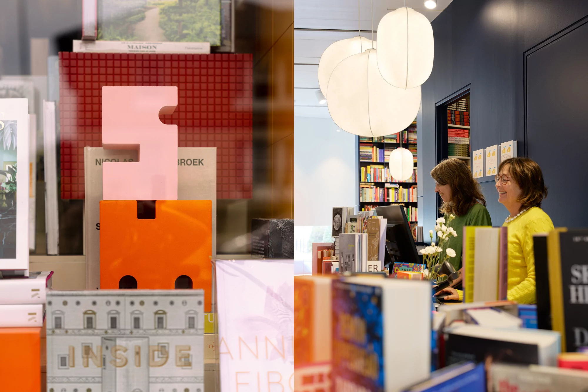 Two women stand behind a counter in a bookstore, browsing the shelves, with artificial lighting and pops of orange and red.