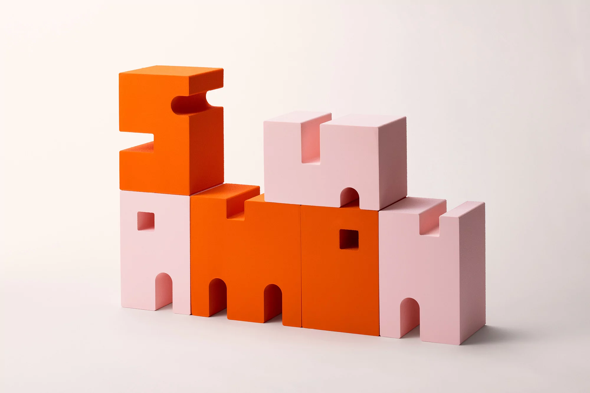 Stacked pink and orange toy blocks create a whimsical, minimalist castle structure against a soft, neutral backdrop.
