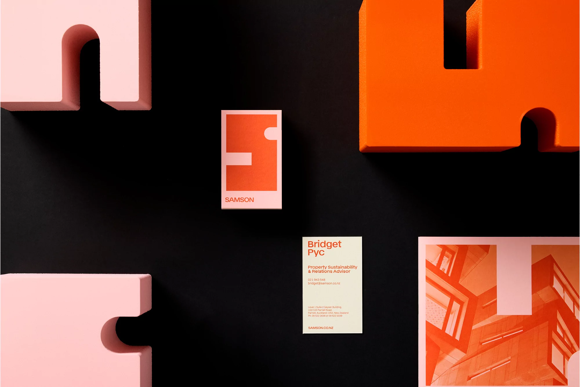 Promotional product shot: business cards, building graphics, and dimensional letter cutouts on a black background.