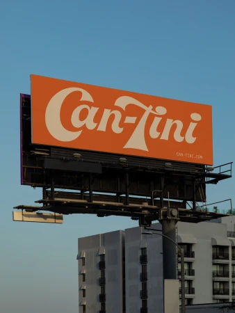 Eye-level, outdoor shot of a large, orange Can-Tini billboard with white retro font against a clear blue sky and buildings.
