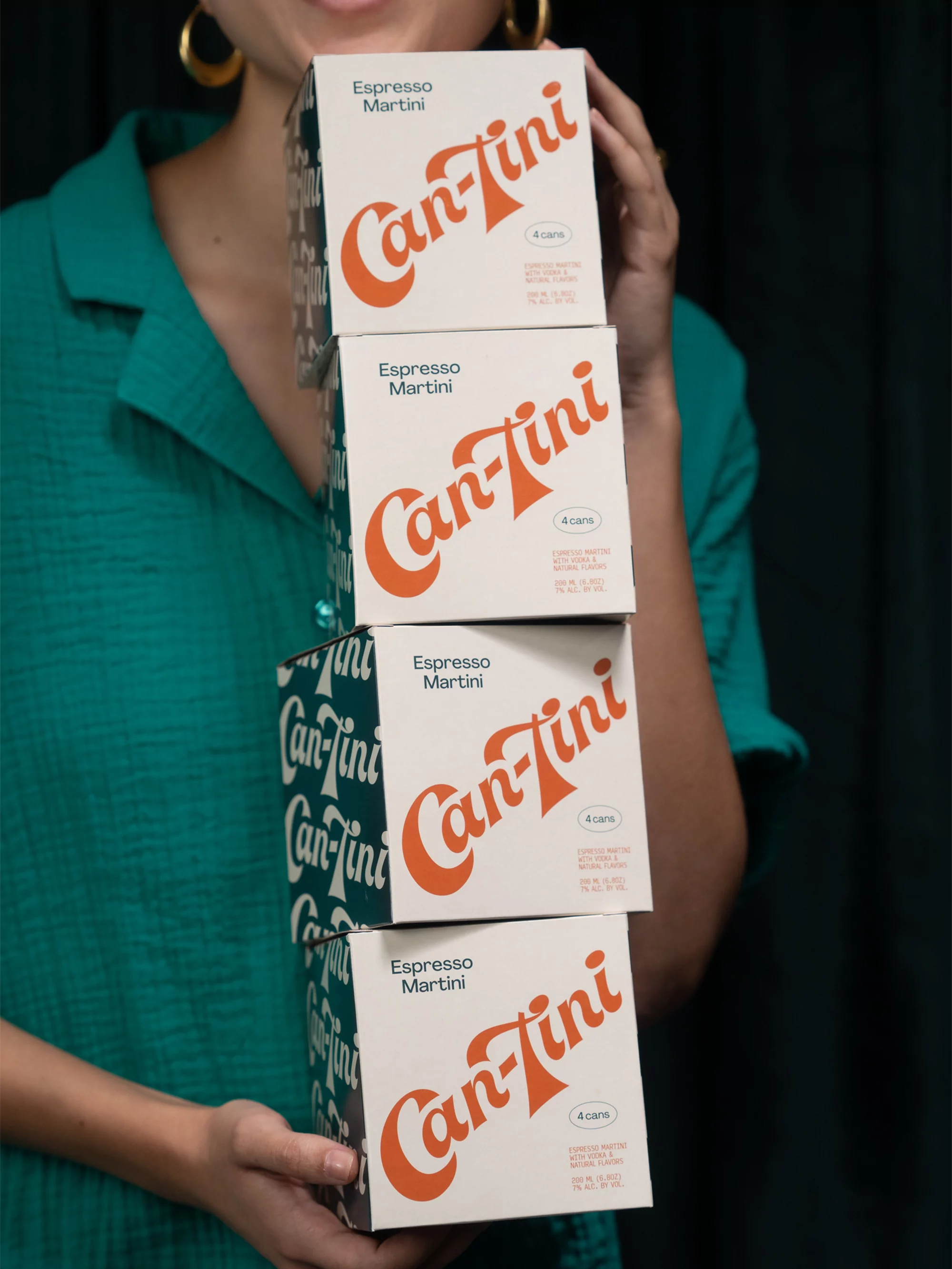 Person holding a stack of four 'Can-Tini' Espresso Martini boxes in a studio setting, with a dark green background.