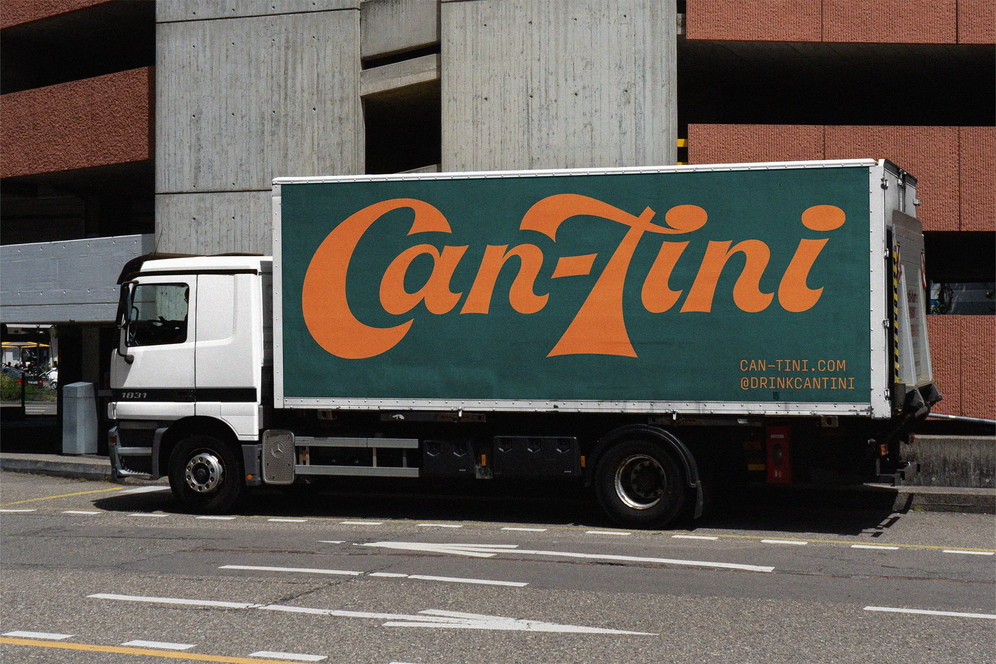 Delivery truck with 'Can-Tini' branding parked on a city street in front of a brick and concrete building on a sunny day.