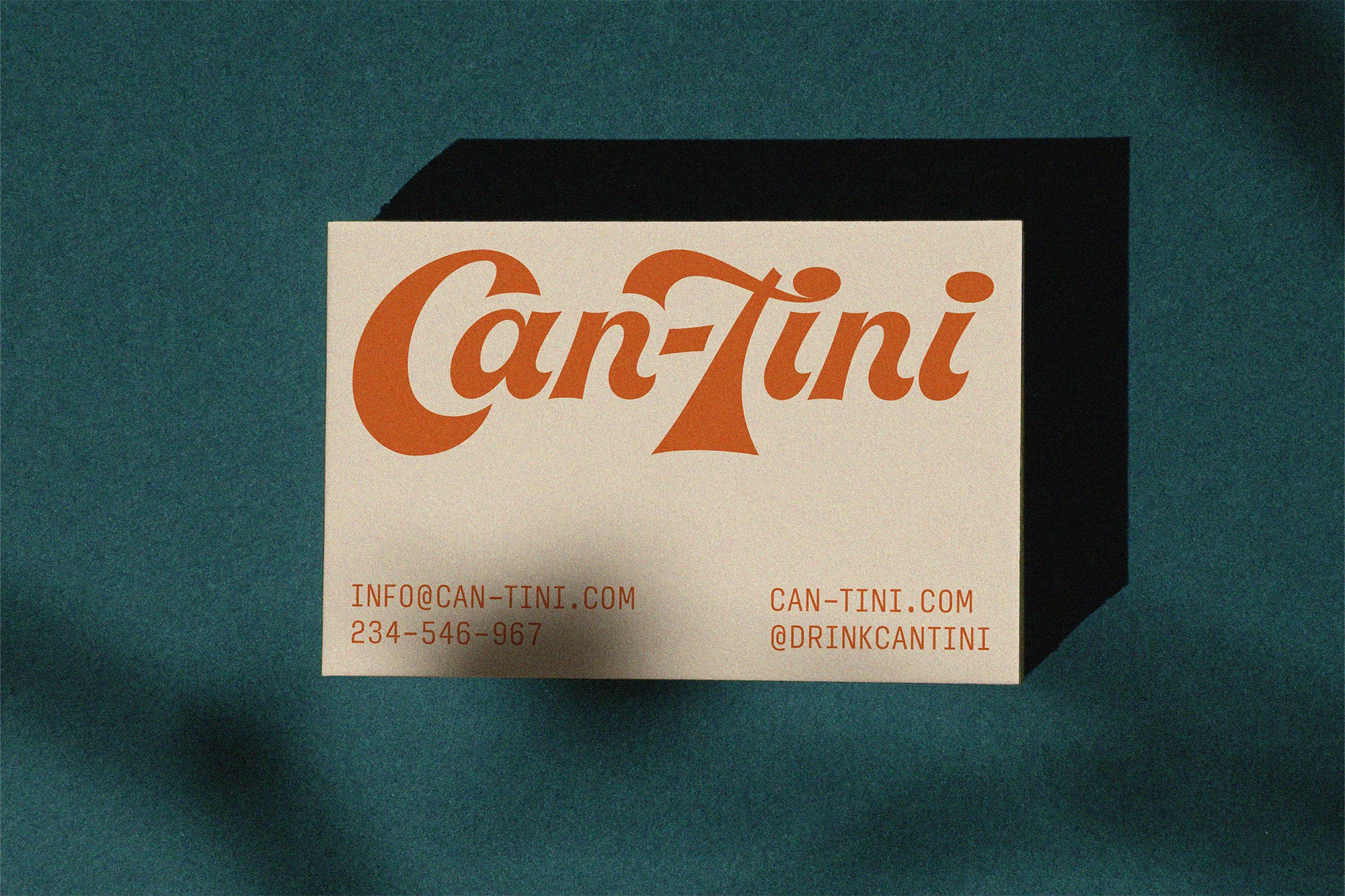 Close-up of a business card with a vintage-style orange logo 'Can-Tini' against a dark teal textured background with soft shadow.