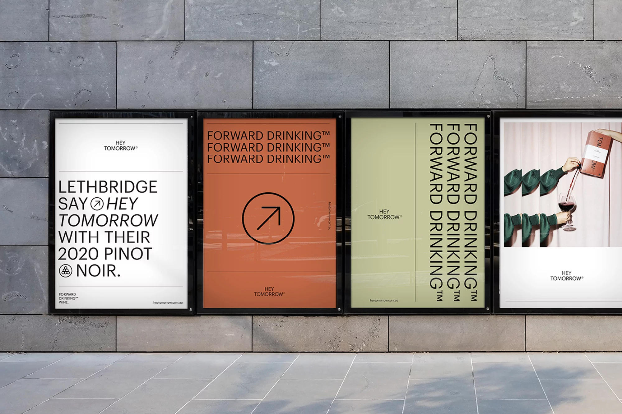 A series of four posters advertising Hey Tomorrow wine, each with unique designs and text, displayed on a gray brick wall.