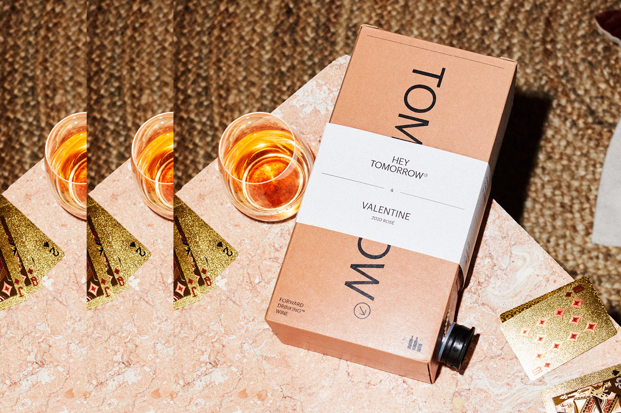 Box of rosé wine on a table with playing cards and wine glasses in a brightly lit indoor setting, drink photography.