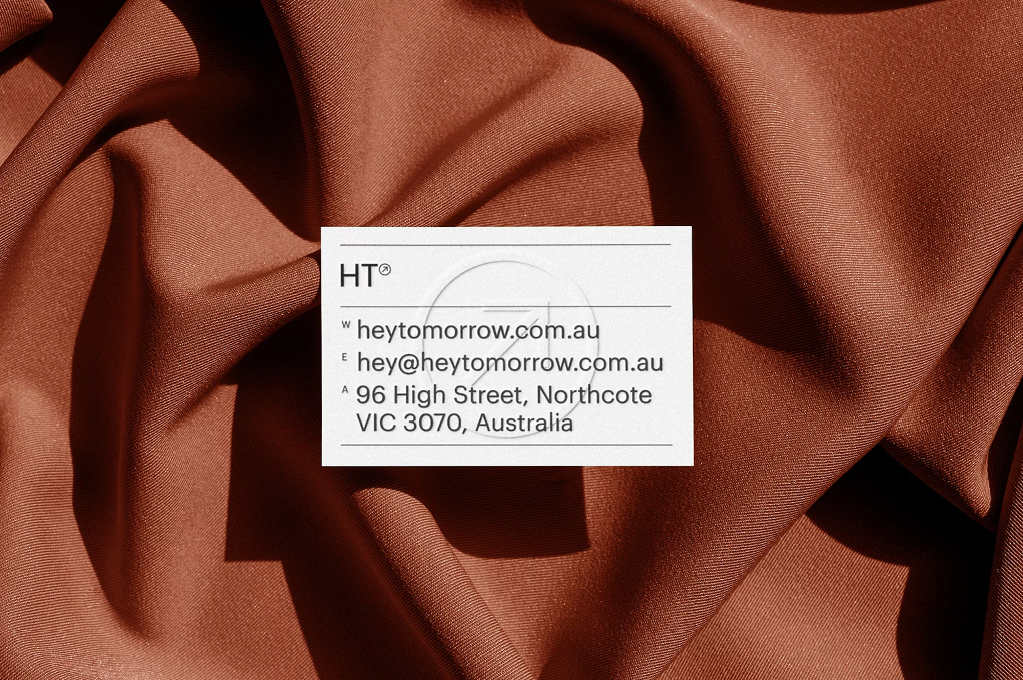 White business card resting on draped terracotta brown fabric background with visible folds and soft lighting.