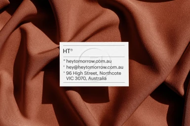 White business card resting on draped terracotta brown fabric background with visible folds and soft lighting.