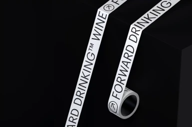 White branded tape with black typography unrolling over dark geometric surfaces
