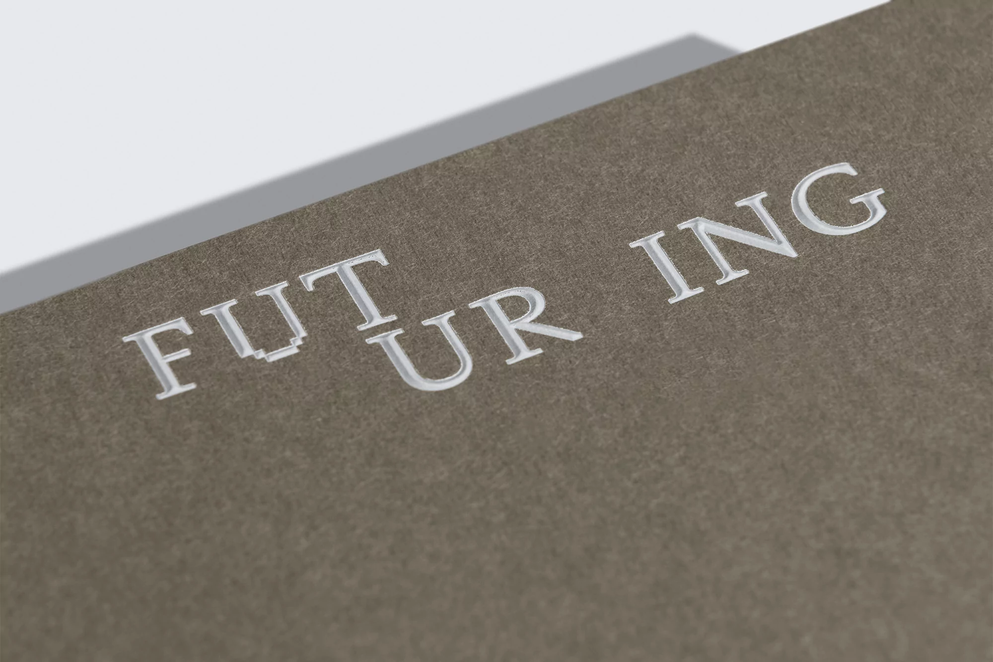 Embossed 'FUTURING' text on a textured taupe surface with soft lighting and a minimalist aesthetic, ideal for design inspiration.