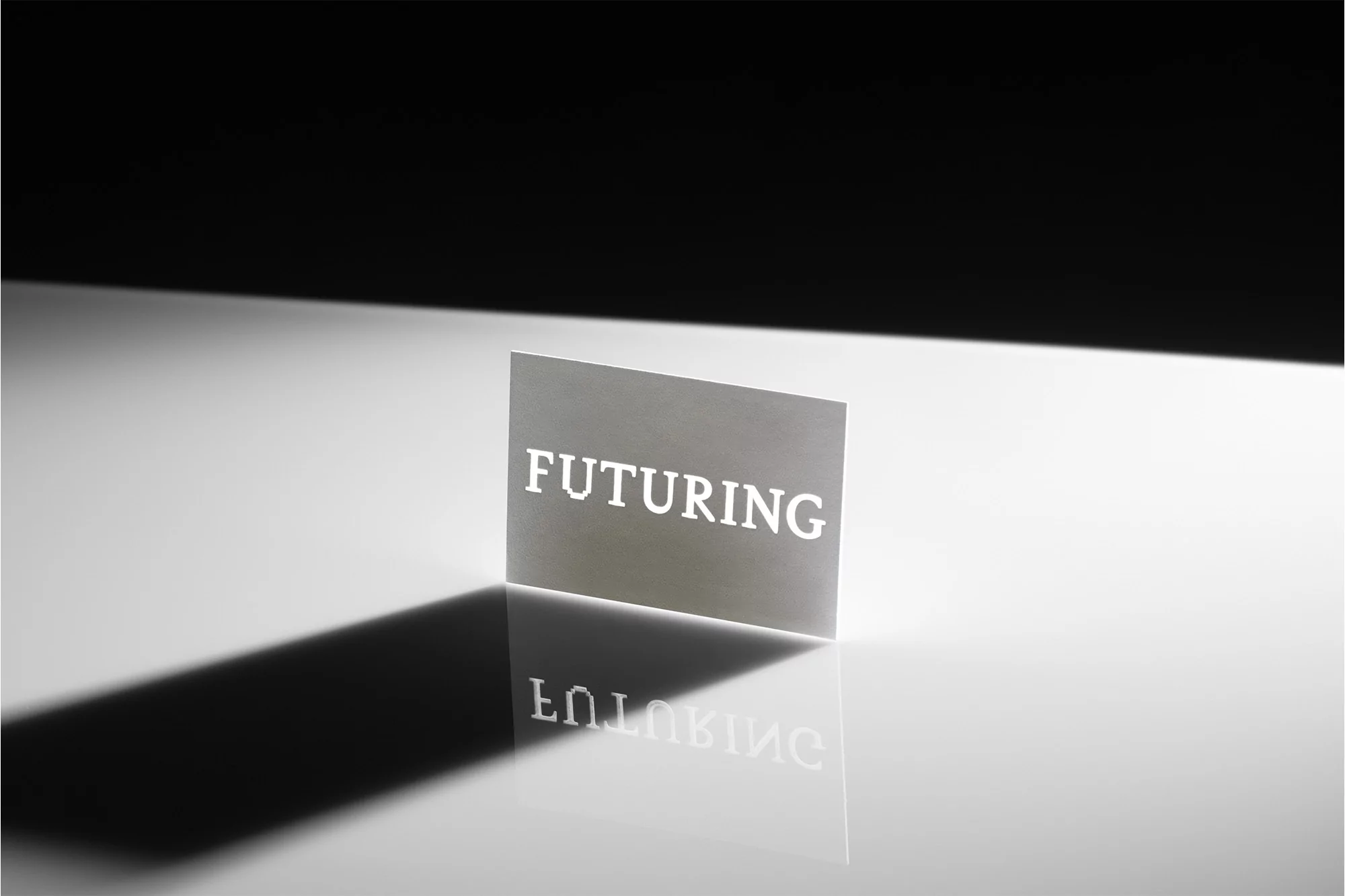 An abstract image featuring a card with the word 'FUTURING' in bold letters, casting a sharp shadow on a glossy surface against a dark background.