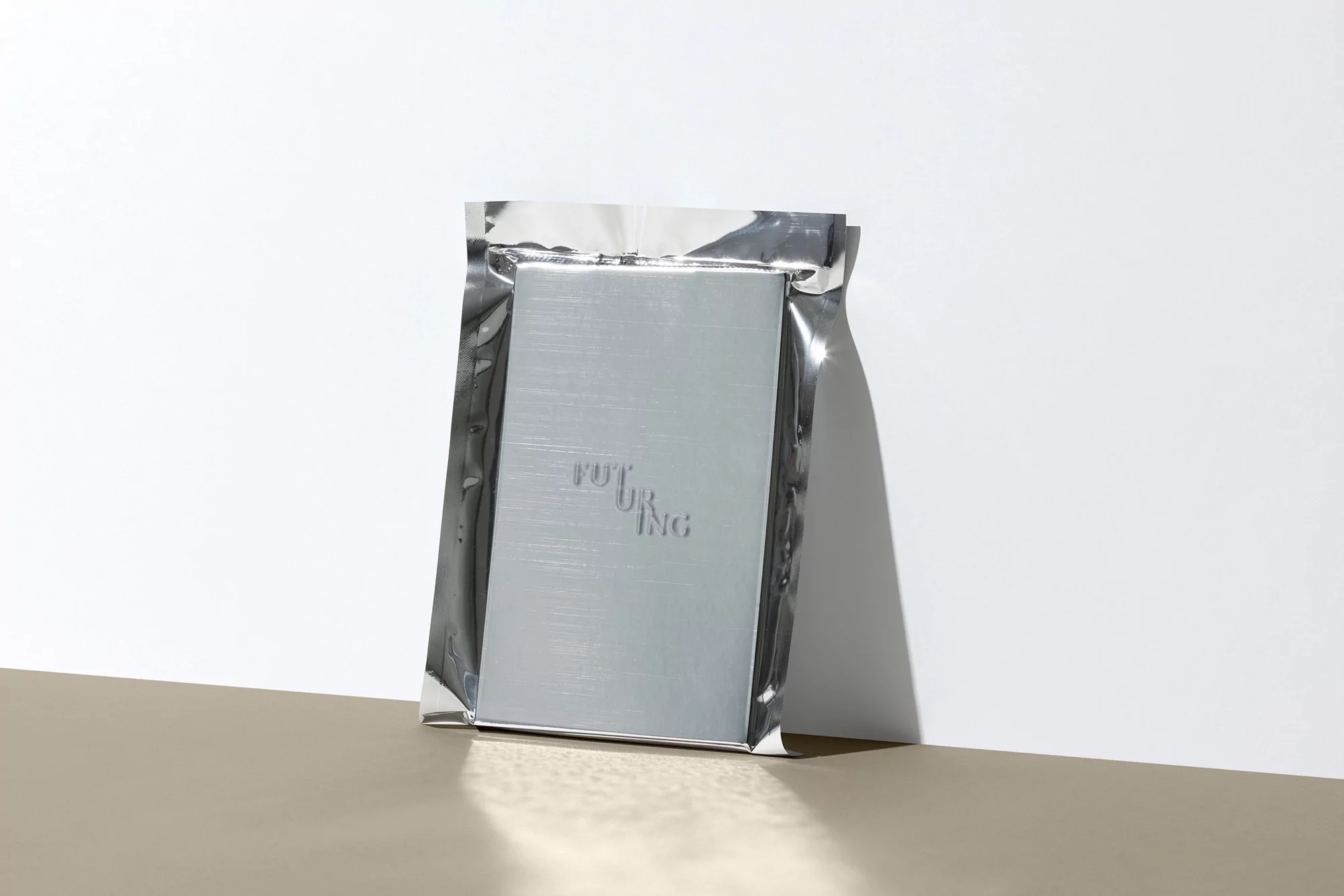 Shiny foil package featuring a silver card with the text 'Futuring' inside, photographed in a studio with neutral background and hard light.