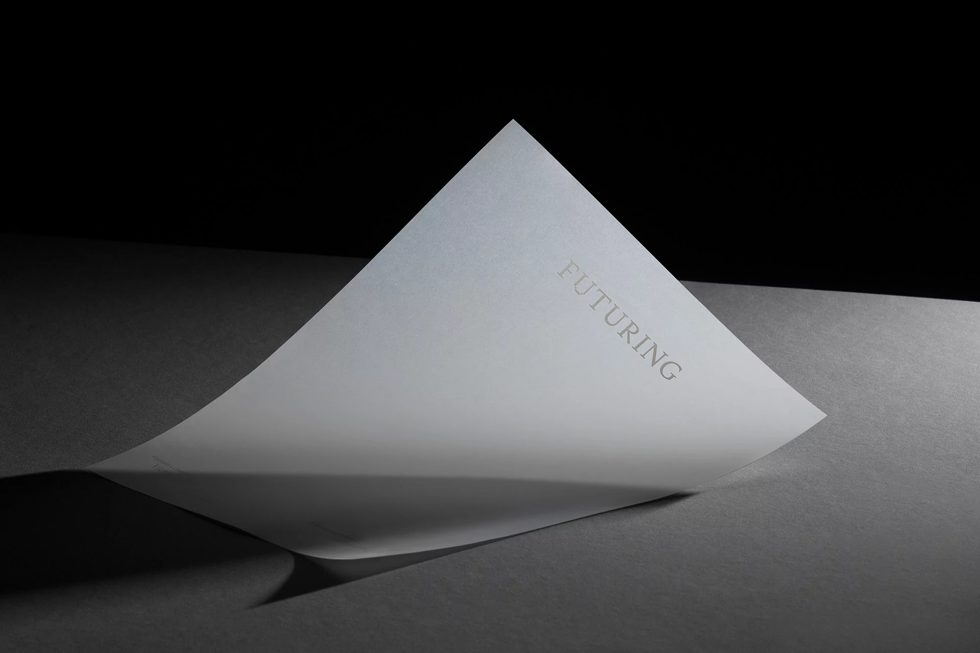 Abstract shot of a white paper with 'FUTURING' text, angled on a dark gray surface, creating a sense of dimension and mystery.