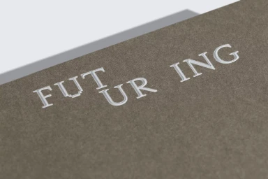 Embossed Futuring brand typography on dark brown textured paper with sharp angled lighting creating subtle shadows.