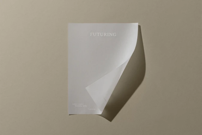 A curled white sheet of paper featuring Futuring branding rests against a minimalist taupe textured background casting a dark shadow.