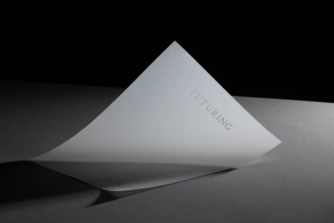 Curved white sheet of paper bearing the Futuring brand name displayed on a dark surface under dramatic studio lighting.