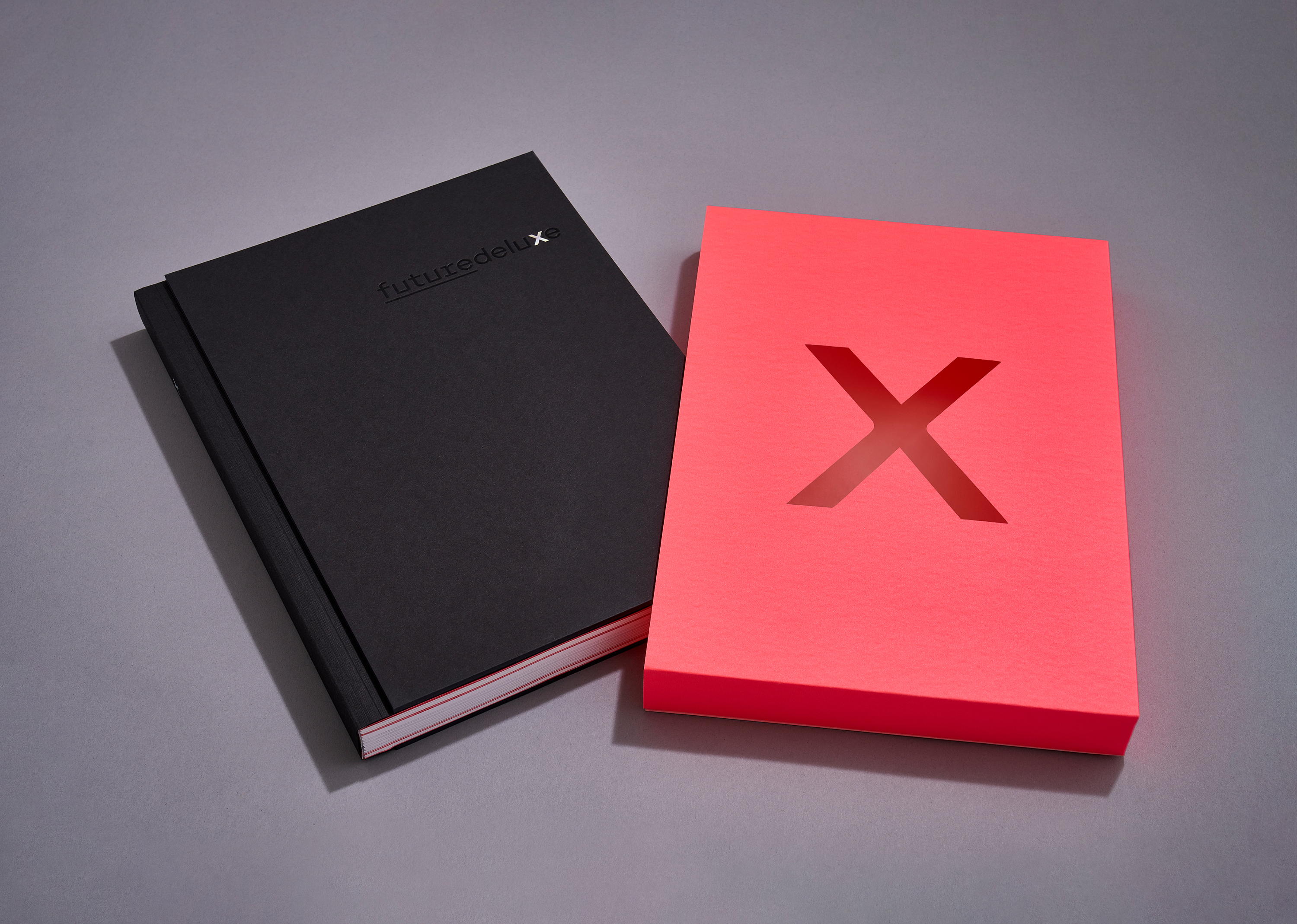 A black book and a red box with the letter X on a gray surface, providing a simple product-style shot against a neutral background.