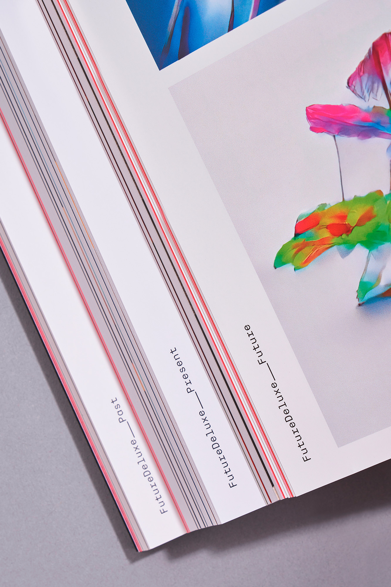 Close-up angled shot of open printed magazine pages featuring FutureDeluxe brand identity on white paper stock with colourful artwork.