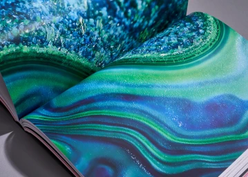 An open magazine or book displaying vibrant blue and green abstract mineral patterns across glossy pages.